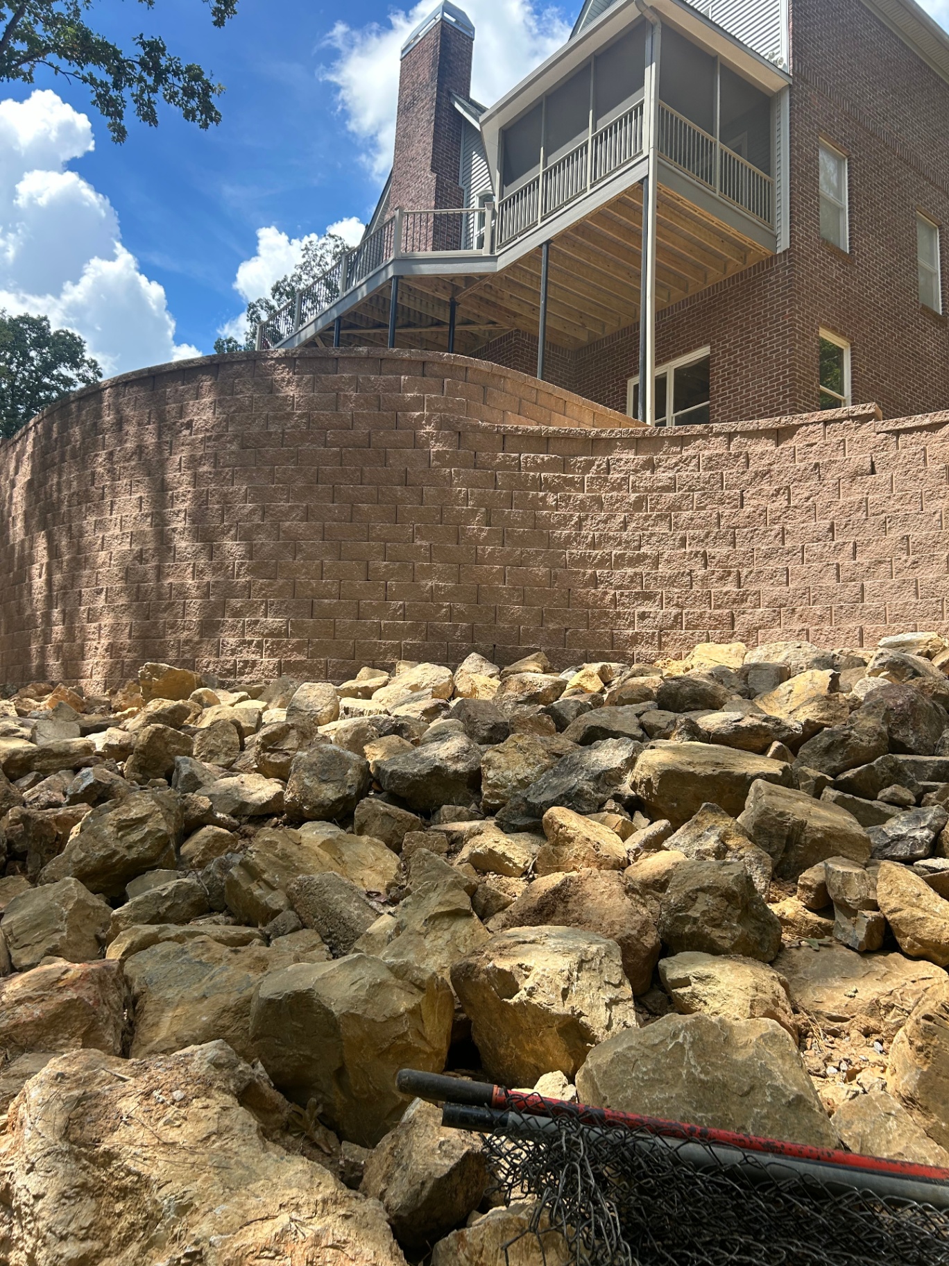 Tall curved retaining wall with boulders below a brick home