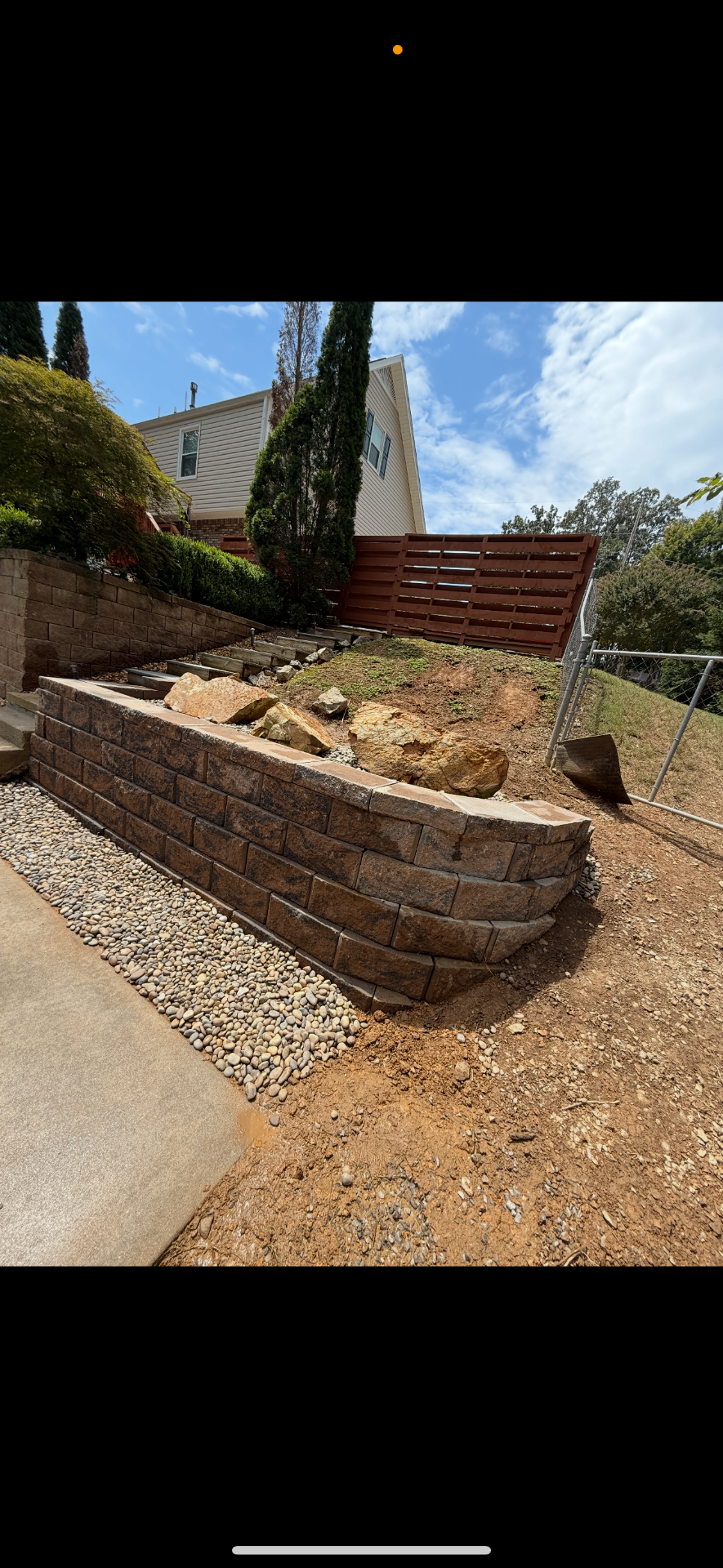 Curved brown block retaining wall with gravel drainage beside a sloped yard